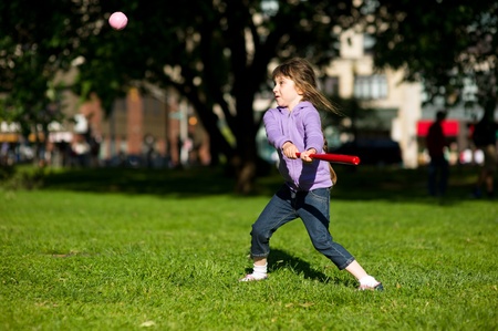 Child girl playing baseball in park on a bright summer dayの写真素材