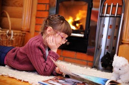 Child girl is reading a book in front of fireplaceの写真素材