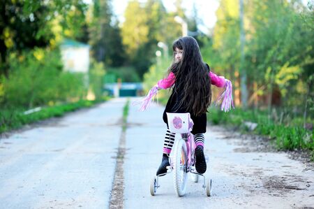 Fancy little girl with long hair riding her pink bikeの写真素材