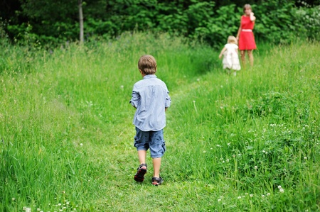 Child boy walking on meadow towards his familyの写真素材