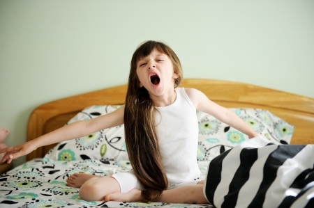 Portrait of little girl sitting in bed in early morningの写真素材