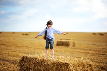 Little girl standing on a top of big haystack in the middle of the fieldの写真素材