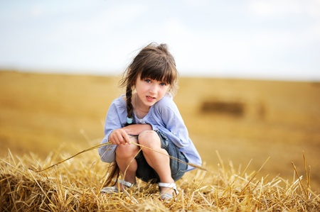 Little girl sitting on a top of haystack in the middle of the fieldの写真素材