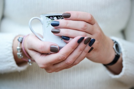 A cup of coffee in woman's hands with blue and brown manicure holdingの写真素材