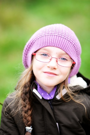 Autumn close-up portrait of little girl in glasses wearing pink hatの写真素材