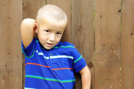 Portrait of little boy posing outdoors in front of wooden fenceの写真素材