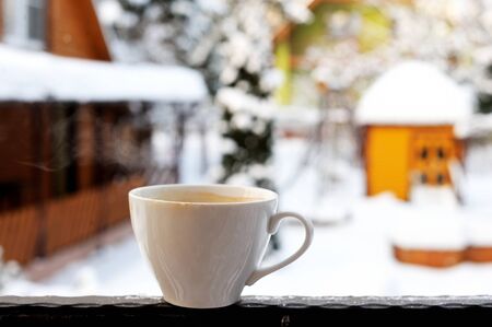 Cup of steamy cappuccino on railing with winter backgroundの写真素材