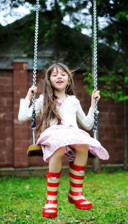 Elegant child girl in countrylike dress and red gumboots swinging in the parkの写真素材
