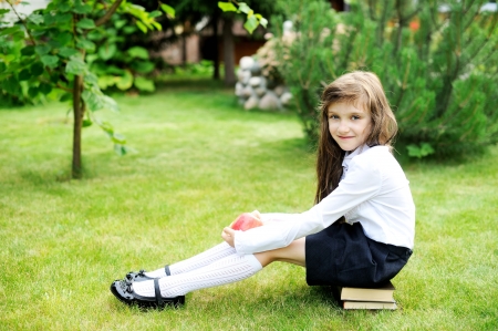 Young girl in school uniform sitting on stack of books