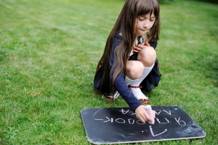 Nice young girl in navy school uniform writing on chalkboard in russianの写真素材