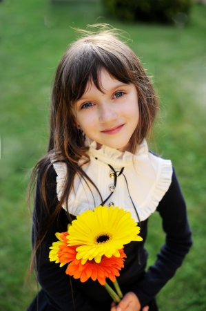 Young girl in navy school uniform posing with yellow and orange flowersの写真素材