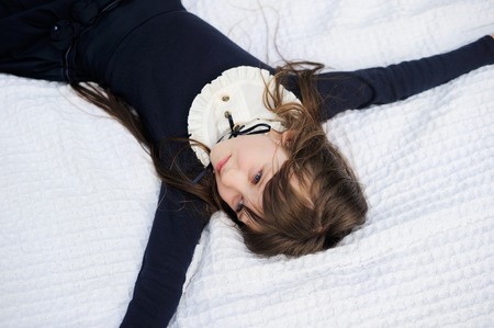 Portrait of young girl in navy school uniform relaxing on white blanketの写真素材