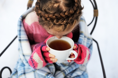 Child girl wrapped in warm blanket drinking hot tea outdoorsの写真素材