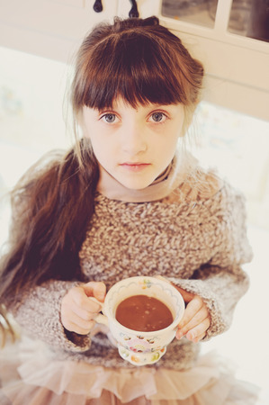 Child girl holding a vintage cup of hot drink, sepia tone addedの写真素材