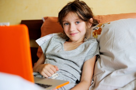Smiling young teenager lying on her bed and using a laptopの写真素材