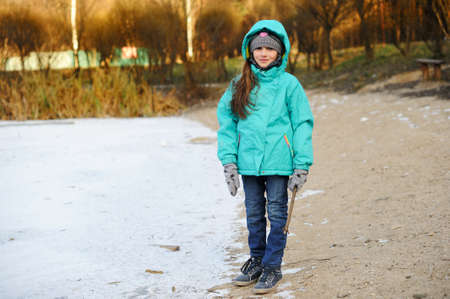 Cute child girl in jeans and colorful jacket walking in snowy winter parkの写真素材