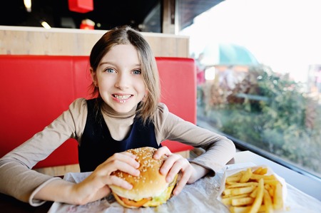 Cute little girl in school uniform eating a hamburger and potatos in the restaurantの写真素材