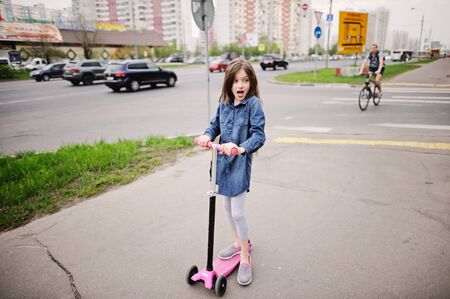 School aged little girl in dress on the scooter in the city streetの写真素材