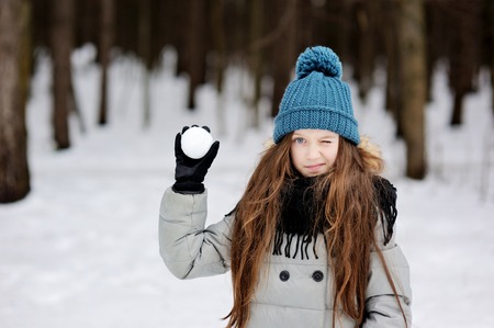 Funny little girl having fun in beautiful winter park with snowballsの写真素材