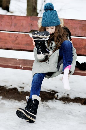 Funny little girl having fun in beautiful winter park and put off snow from the bootsの写真素材