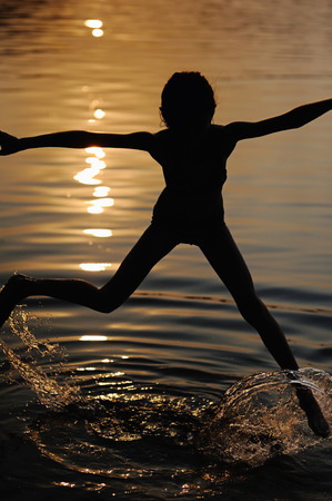 Dance and jump kid girl in the water on the sunset, silhouetteの写真素材