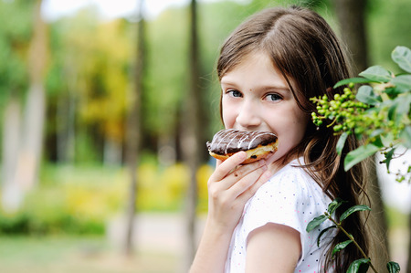 Cute kid girl eating sweet donut outdoor in the park on sunny warm dayの写真素材