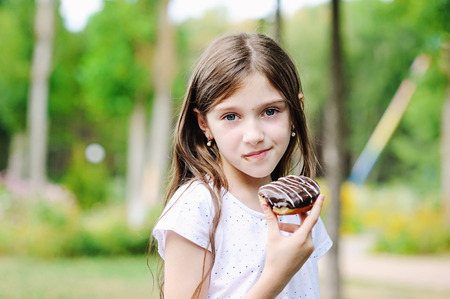 Cute kid girl eating sweet donut outdoor in the park on sunny warm dayの写真素材