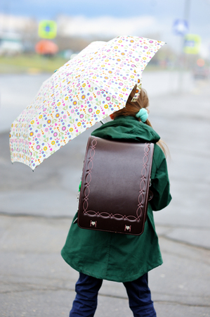 Adorable, elegant school aged kid  girl ,holding colorful umbrella walking in the city street in rainy dayの写真素材