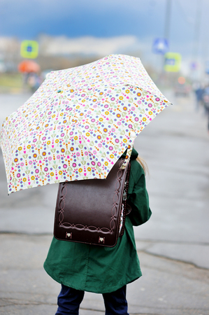 Adorable, elegant school aged kid  girl ,holding colorful umbrella walking in the city street in rainy dayの写真素材