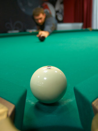 Billiard-ball at the pocket on the green table and man, striking the ball