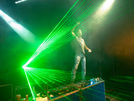 DJ with upraised arm standing on the table near the music control panel in the green laser raysの写真素材