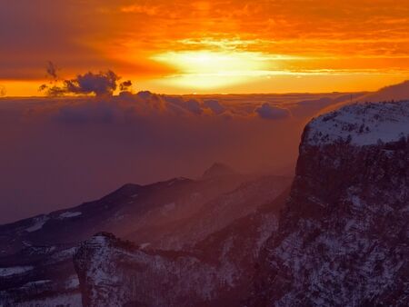 Winter sunset over the mountains with clouds and fogの写真素材