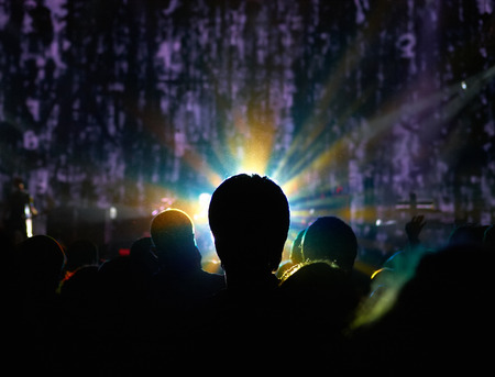 Silhouette of man standing in a crowd with halo around the head in front of stage with abstract backgroundの写真素材