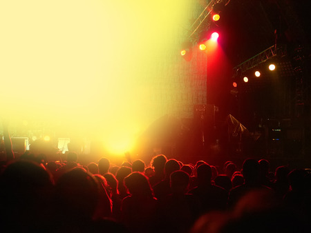Silhouettes of cheering people backlit by big red spotlight at rock concert in front of illuminated stageの写真素材