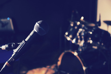 Vocal microphone with stand on the stage with blurred drum set in the background, blue toned imageの写真素材