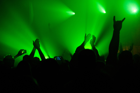 Silhouettes of people rising up hands in the green fog lit with spotlights beamsの写真素材