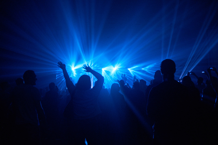 Silhouettes of people with raised hands against spotlights blue light show and musicians on the concert stageの写真素材