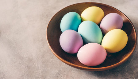 Colorful Easter eggs in a wooden bowl on a gray background.の素材