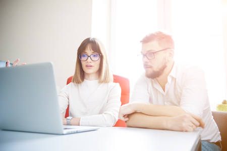 Two young coworkers dressed casual using laptop in white interiorの写真素材