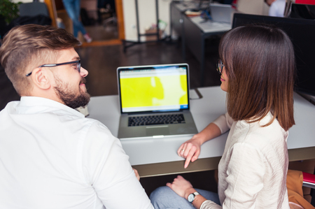 Two young coworkers dressed casual using laptop in white interiorの写真素材