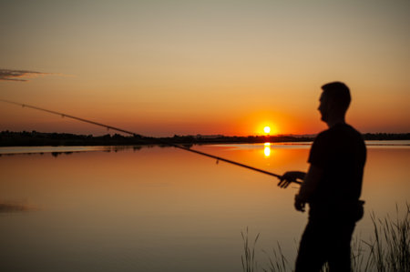 Silhouette of a man fishing on the lake at sunset.の写真素材