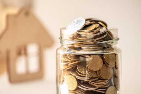 Coins in a glass jar with a wooden house on the backgroundの写真素材