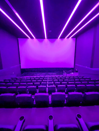 Purple cinema auditorium with seats and projector screen, purple lights