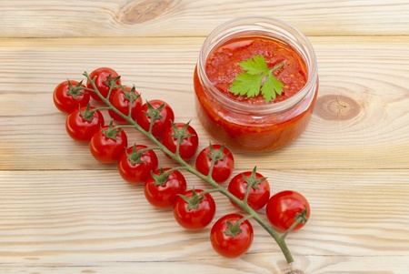Red tomatoes on a branch and tomato paste in a jar on a wooden table.の写真素材