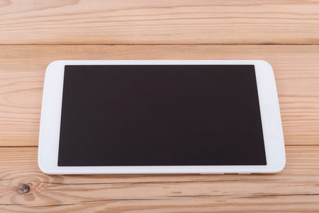 Tablet computer with blank screen on wooden background.