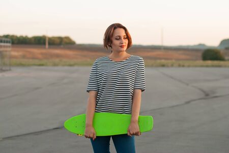 Beautiful young girl in a shirt with a skateboard in hands.の写真素材