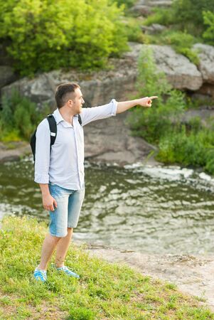 Tourist standing near a mountain river pointing thumb into the distance.の写真素材