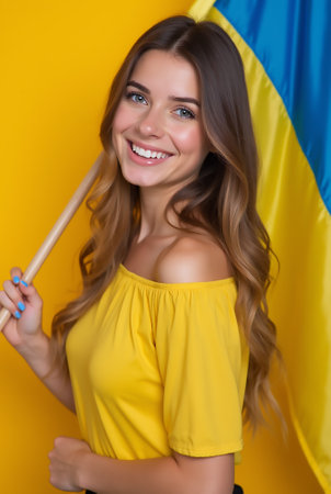 A woman with long hair dressed in a yellow top stands against a bright yellow backdrop, proudly holding a blue and yellow flag, radiating happiness and positivity.の素材