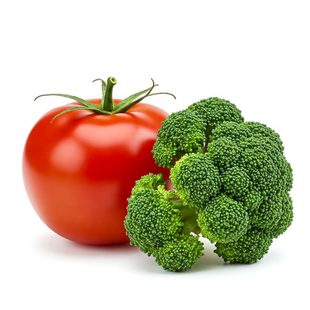 Vibrant red tomato stands next to fresh green broccoli, both showing their natural colors under bright lighting. This arrangement emphasizes the freshness and appeal of vegetables.の素材