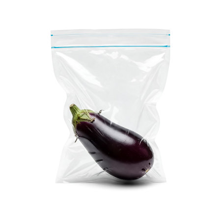 A whole eggplant is placed inside a clear zip-top plastic bag, showing its deep purple skin and glossy texture, prepared for use in various culinary dishes.の素材